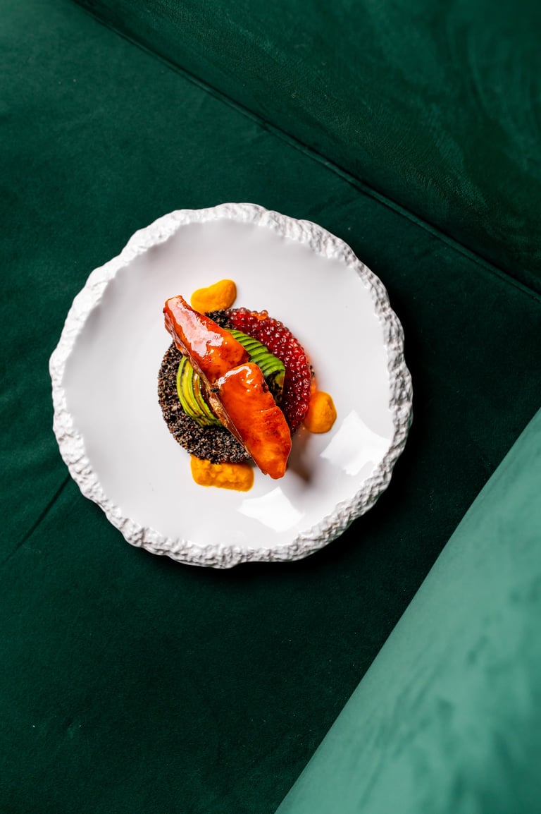 Gourmet dish with plated salmon, red caviar, avocado and sauce on a modern white plate in fine dining style