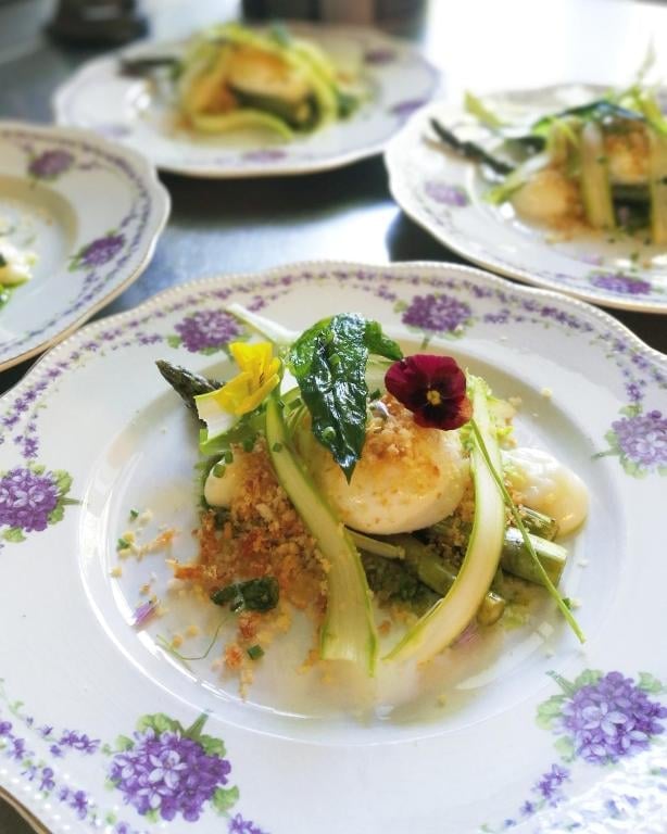 Elegant plated dish with seared scallop, fresh greens, and edible flowers on purple-patterned white dinnerware