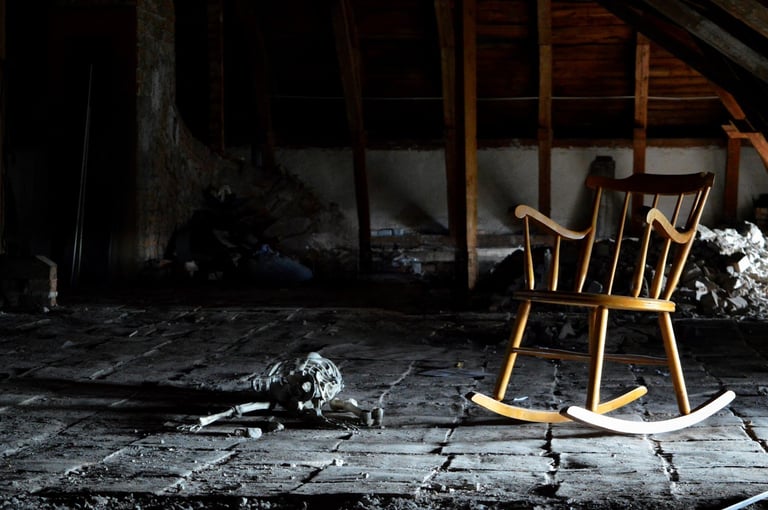 Wooden rocking chair in abandoned, debris-filled room with exposed beams and charred walls