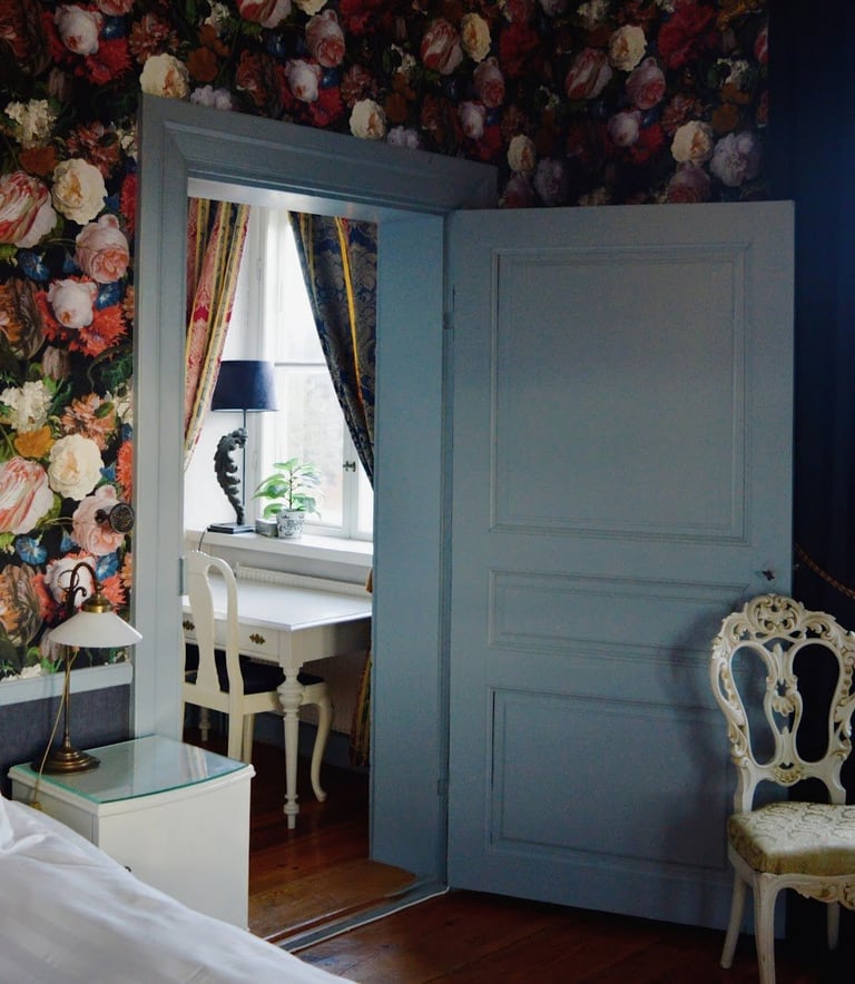 Blue double doors open to a study room with floral wallpaper visible above, showing a desk and ornate white chair beside