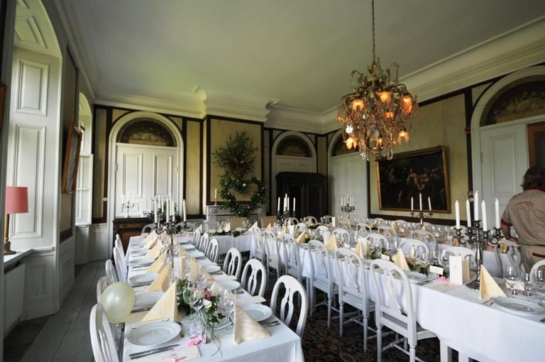 Elegant formal dining room setup with long tables, white linens, ornate chandelier, and classical architectural details.