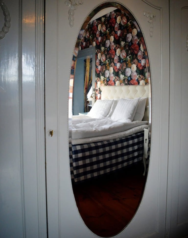 Oval mirror reflecting a bedroom with floral headboard, white pillows, and black-and-white checkered bedding