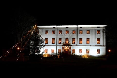 Historic white building illuminated at night with glowing windows and decorative golden lights on surrounding trees