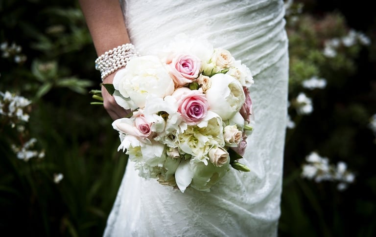 Bride holding a bouquet of white and pink roses with hydrangeas, wearing a beaded bracelet and white wedding dress