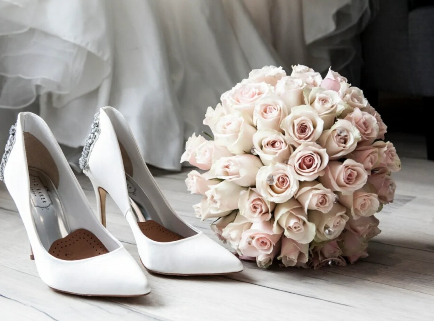 White bridal heels next to a bouquet of blush and cream roses on white floral background