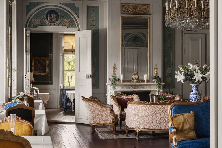 Elegant formal sitting room with ornate furnishings, fireplace with mirror, chandelier, and decorative flowers in blue vases