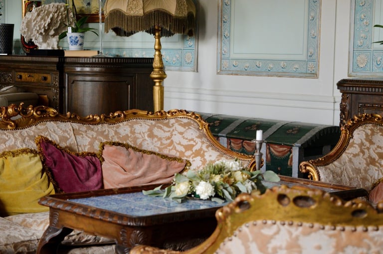 Ornate living room with damask-patterned sofa, decorative pillows, wooden furniture, and traditional decor including a marble table with white flowers.