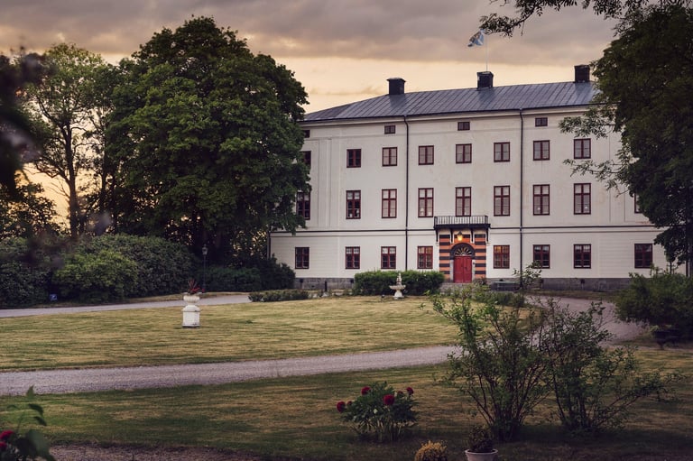 White neoclassical mansion with red entrance door surrounded by green lawns and mature trees at dusk