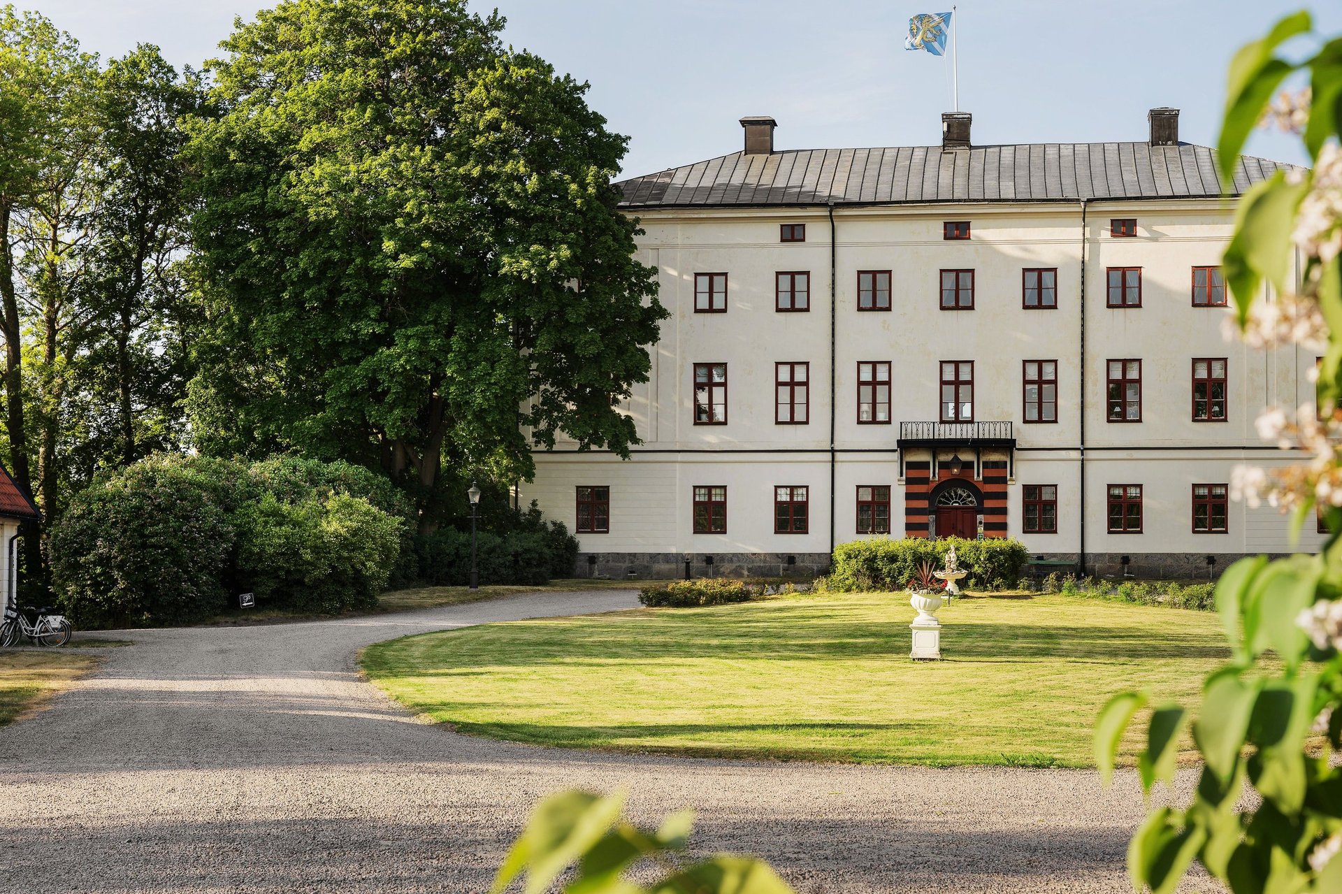 Historic white manor house with metal roof surrounded by manicured lawn and green trees on sunny day
