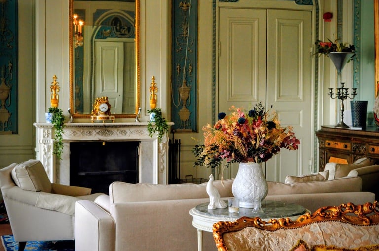 Elegant living room with cream furniture, fireplace with decorative mirror, green walls, white doors, and autumn floral arrangement on side table
