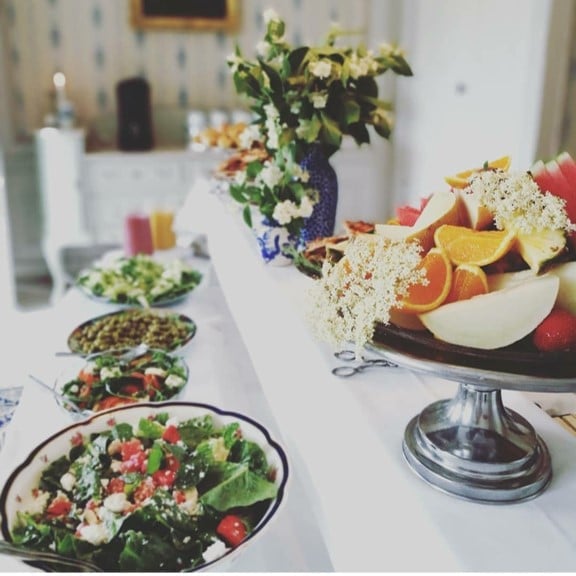 Table setting with fresh salads, fruit platter with citrus slices, and white flowers in a blue vase for an elegant meal