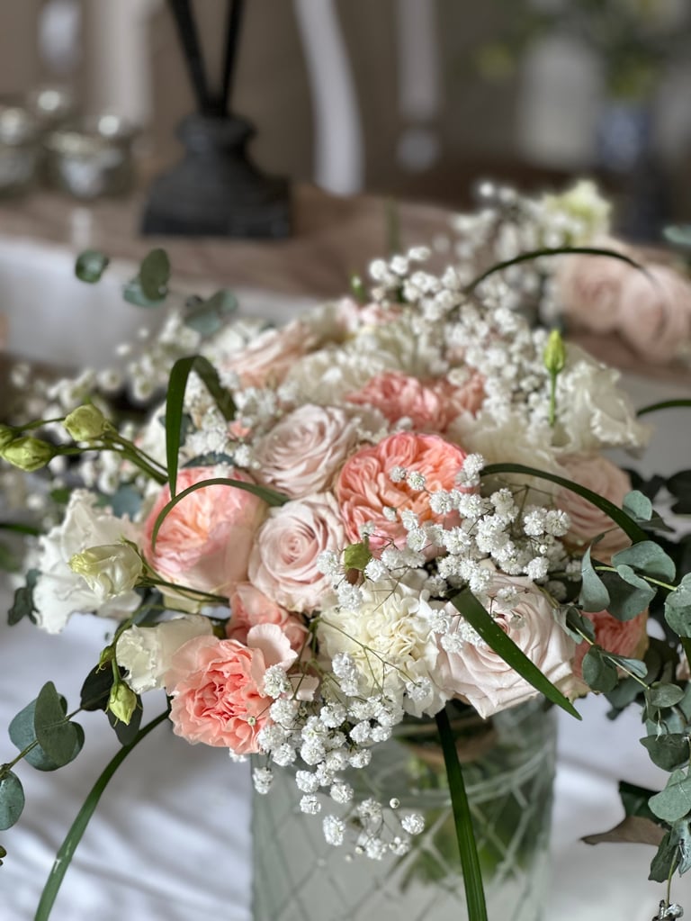 Elegant floral arrangement with pink roses, white babys breath, and green stems in a clear vase on a white table