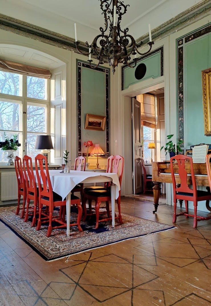 Elegant dining room with red chairs, round table, ornate chandelier, and large mirrors with green walls