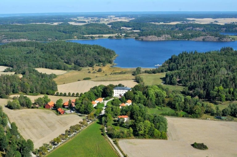 Aerial view of a rural farmland with blue lake, white house, red barn, green fields, and dense forest