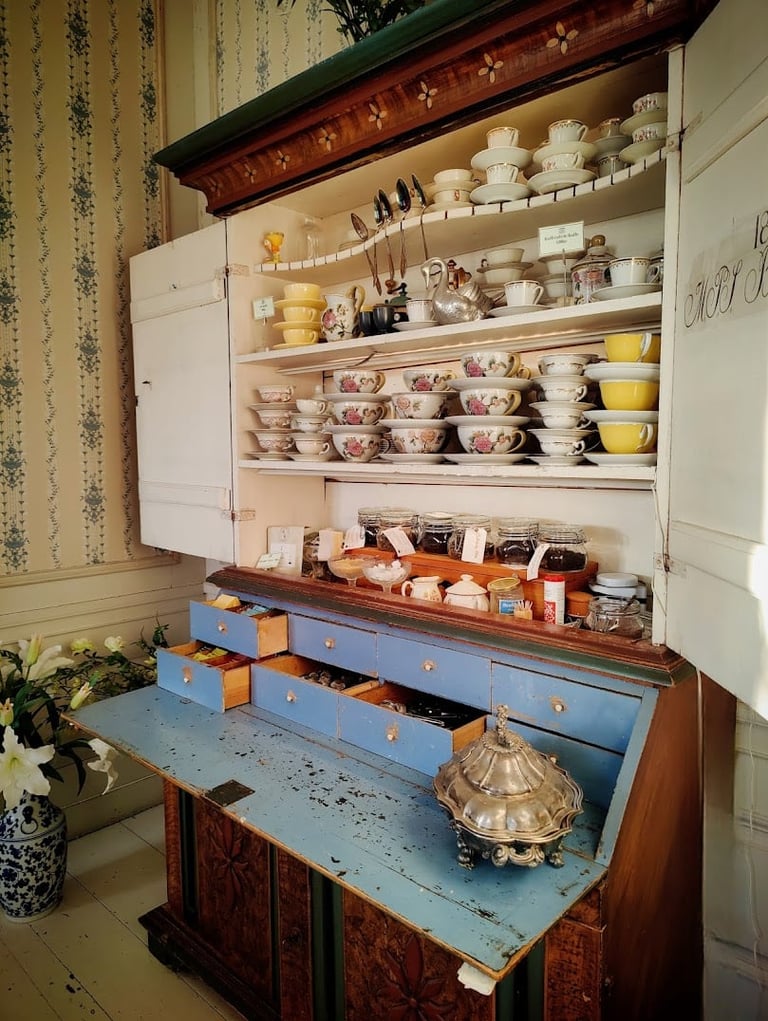 Vintage kitchen cabinet with open shelving displaying decorative dishes, bowls, and kitchenware, with blue drawers and wooden inlay details